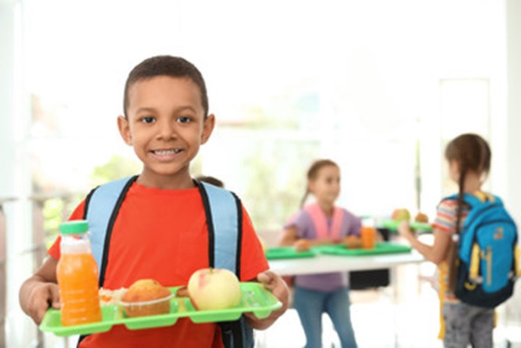 Child smiling and holding his cafeteria lunch at school.