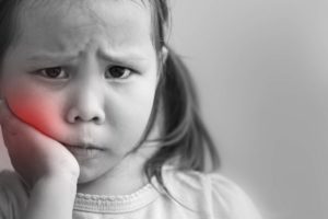 Child holding their cheek in pain 