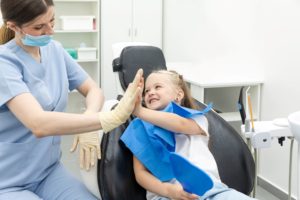 Girl in white shirt sitting in dentist's chair high-fiving a dentist in blue scrubs with white gloves
